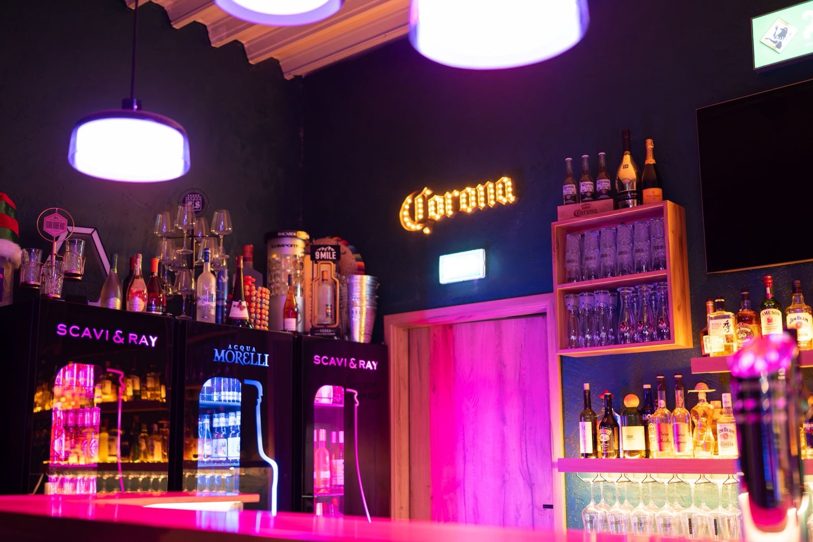 Bar mit Corona-Leuchtschild, Scavi & Ray und Flaschenregal