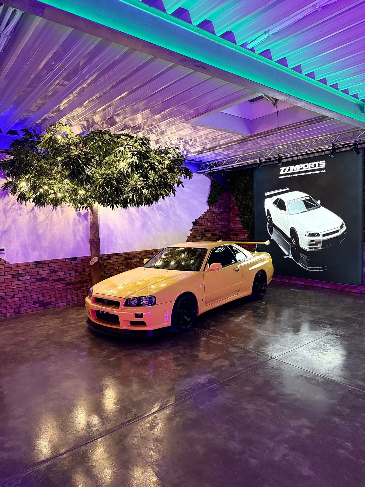 JDM Showroom mit gelbem Nissan Skyline R34 und weißem GT-R unter Kirschblütenbaum