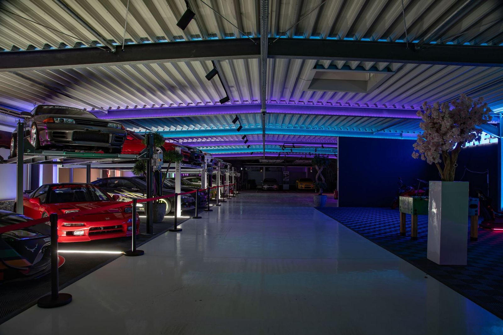 JDM Showroom mit Sportwagen auf Hebebühnen und blauer Neonbeleuchtung
